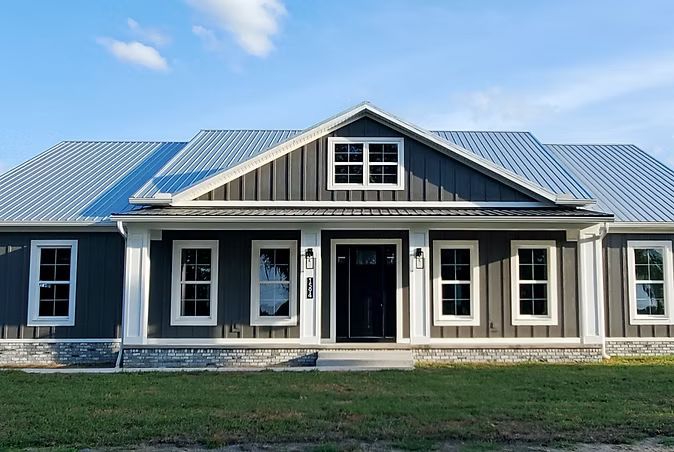 Modern farmhouse exterior with gray siding, blue metal roof, and covered front porch
