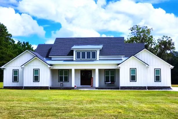 White house with a dark roof and green shutters on a grassy lawn under a blue sky
