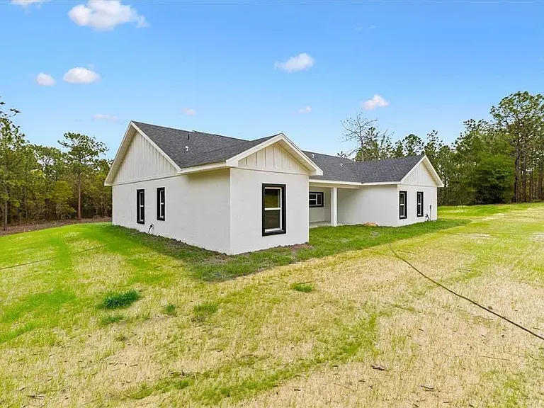 White single-story house with dark roof on a grassy lot under a blue sky