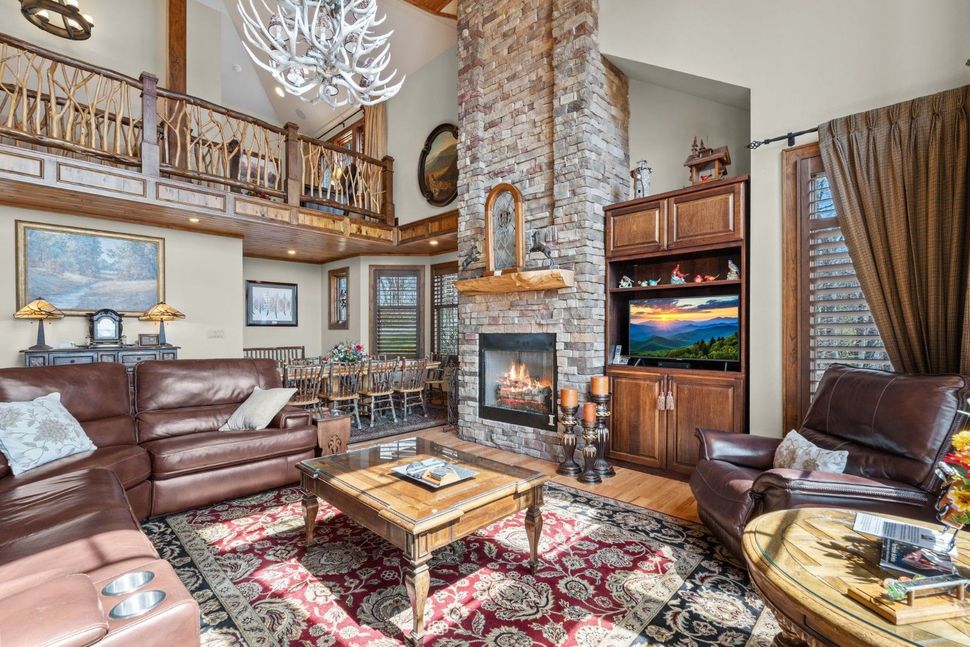 Spacious rustic living room with leather sofas, stone fireplace, loft railing, and large TV by the window
Fox Ridge Retreats; Mountains