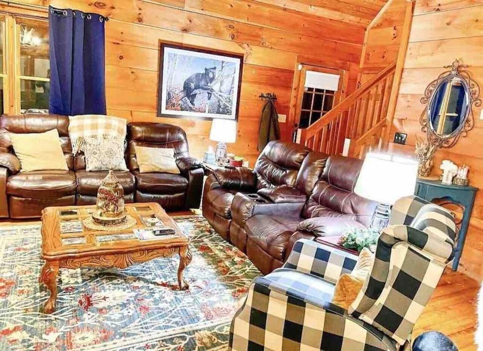 Cozy log cabin living room with leather sofas, plaid chair, rustic coffee table, and framed wall art; Mountains; Fox Ridge Retreats; Rental