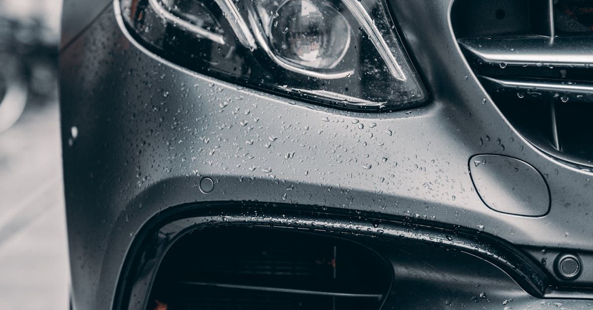 A close up of the front of a car with water drops on it.