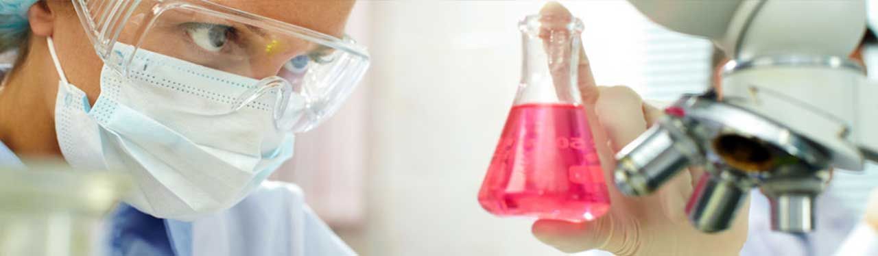 Un científico mira a través de un microscopio un vaso de líquido rosa.