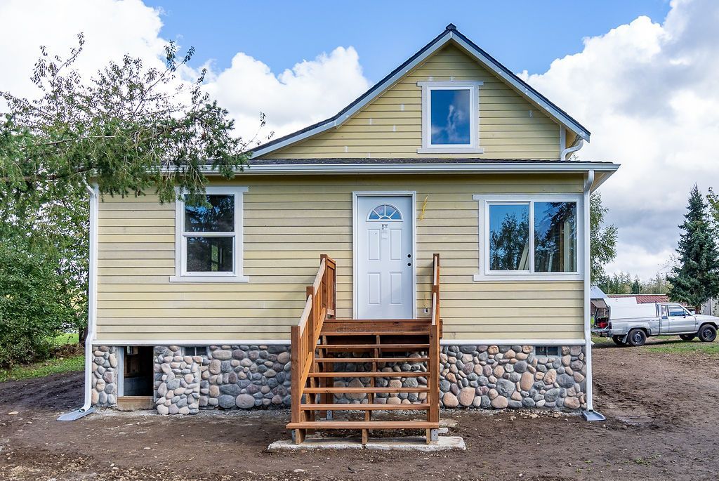 Yellow house with stone foundation, wooden stairs, and a white door under a blue sky.