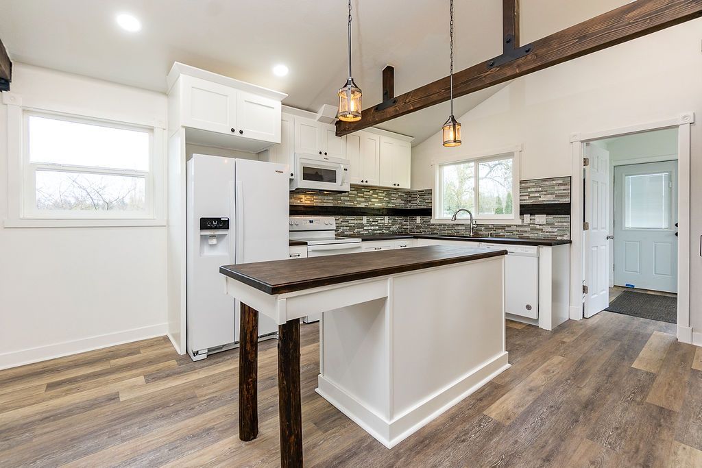 White kitchen with wood island, cabinetry, and flooring. Rustic beams and pendant lights.