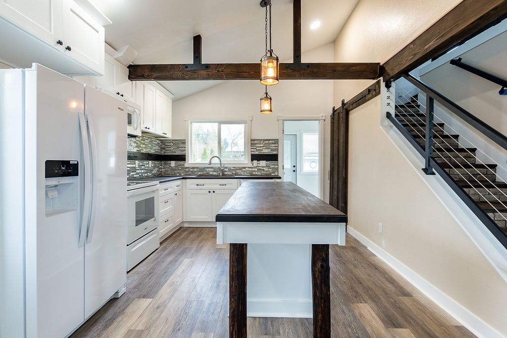 Kitchen with white cabinets, wood island, and staircase.