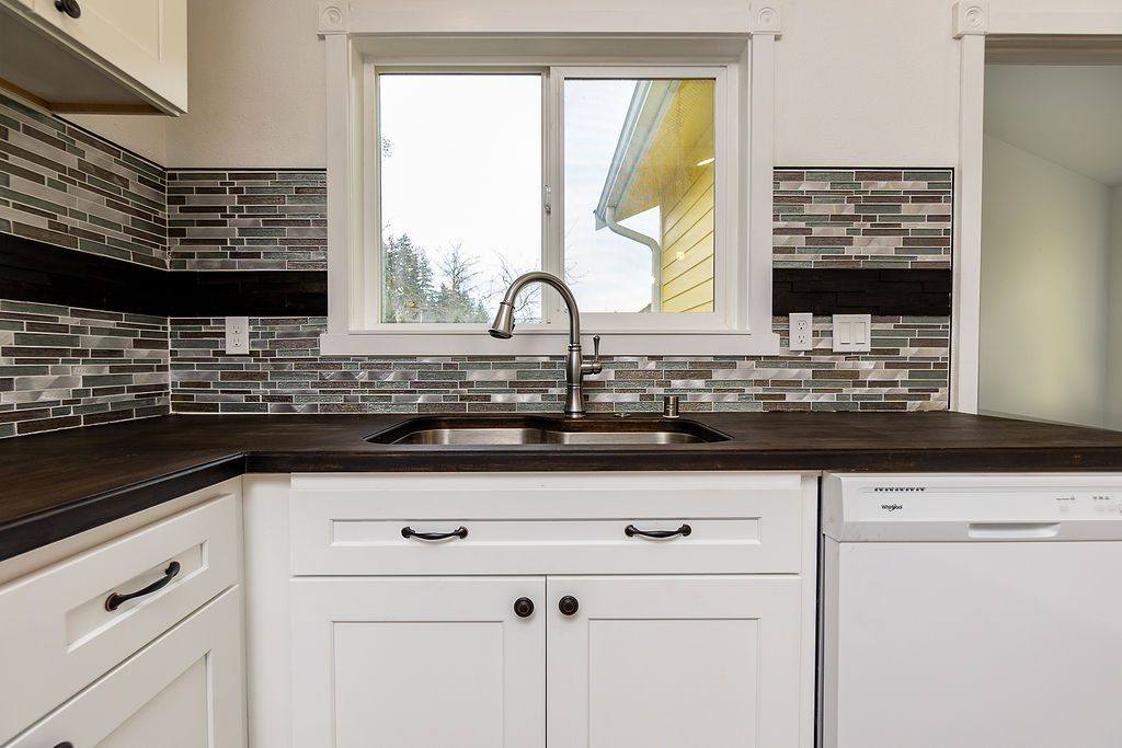 White kitchen cabinets with dark countertop, stainless steel faucet, and window.