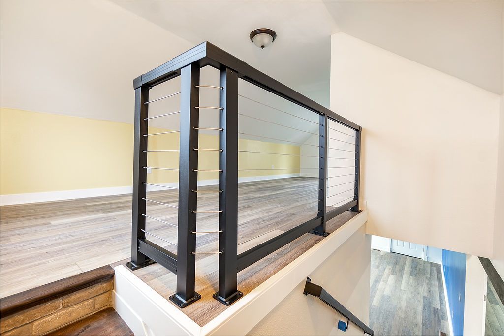 Black metal and glass railing on a second-story loft, light wood floors, neutral walls.