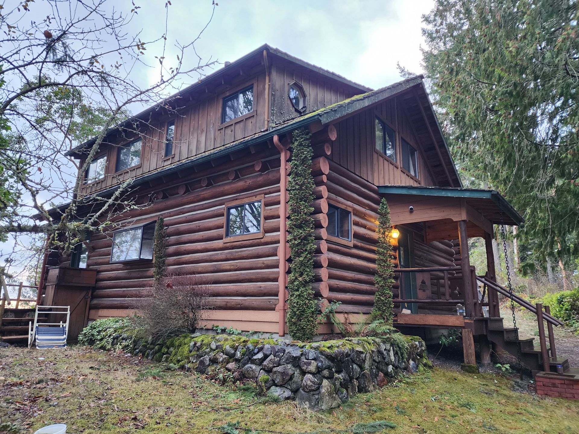 Rustic wooden cabin with a porch, surrounded by trees, under a cloudy sky.