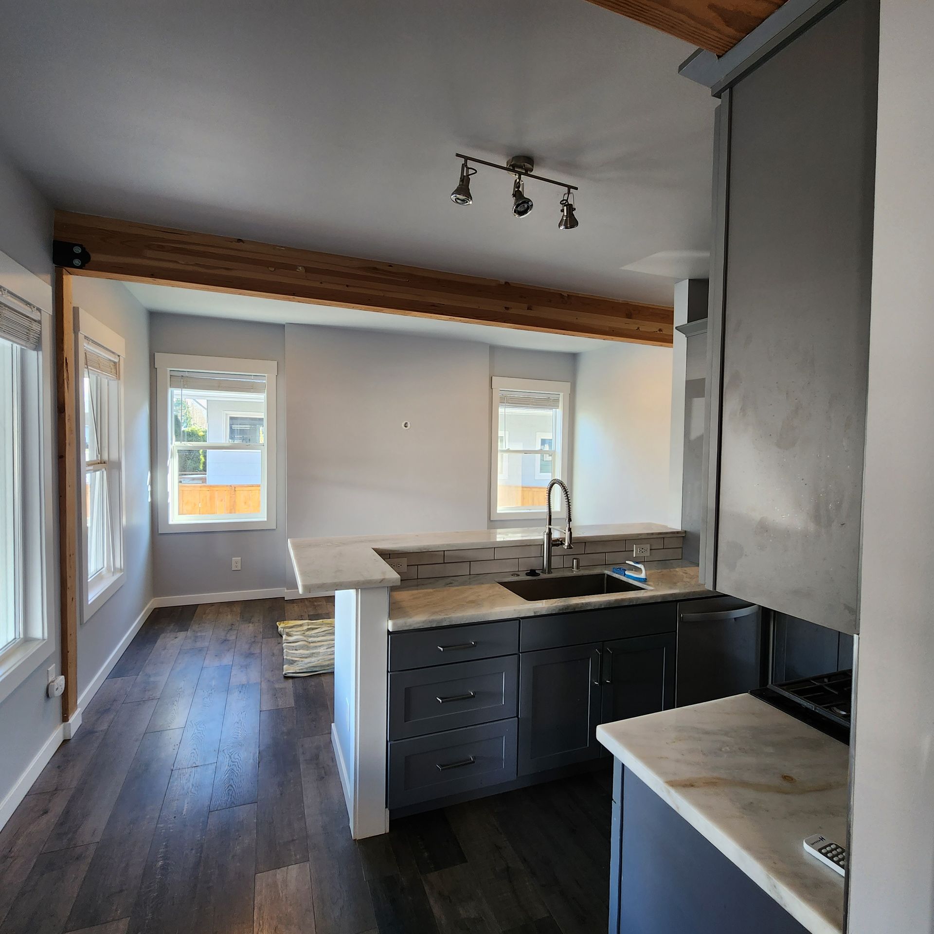 Modern kitchen with dark cabinets, marble countertops, and exposed wooden beam.