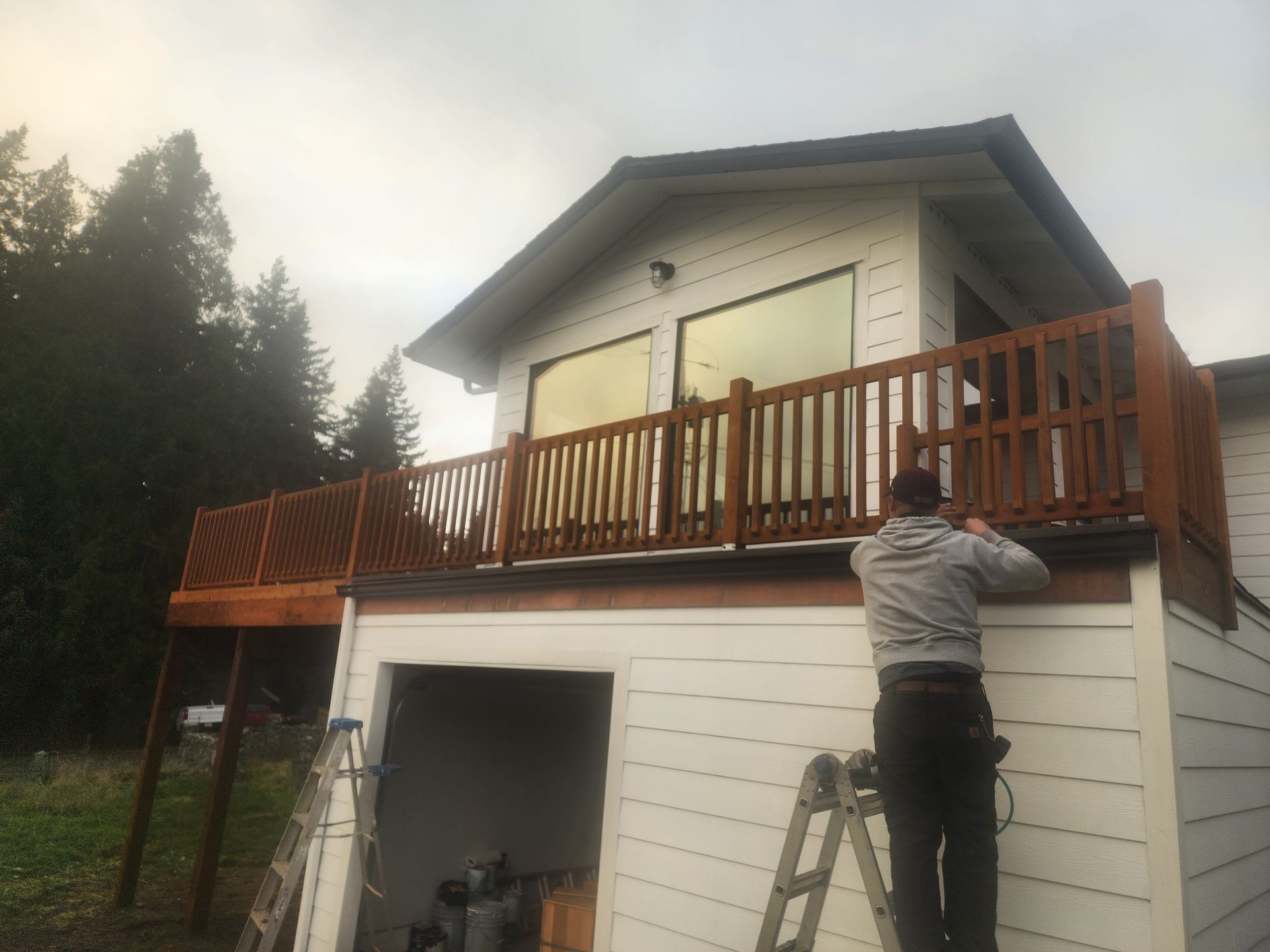 Person on a ladder working on a wooden deck on a white house.