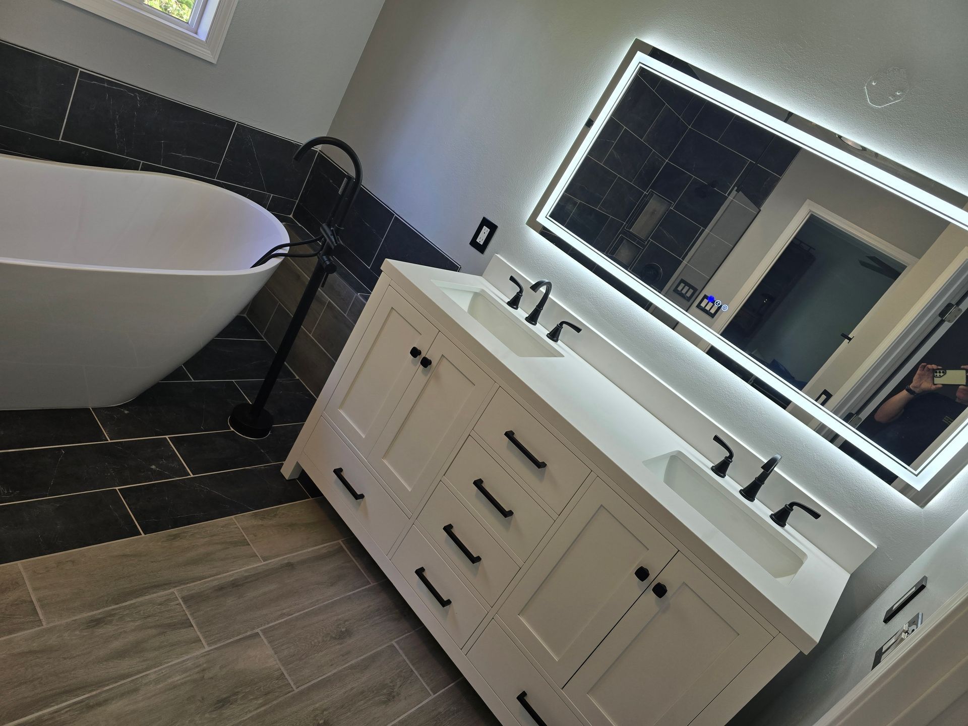 Modern bathroom with white double vanity, lighted mirror, and freestanding tub.
