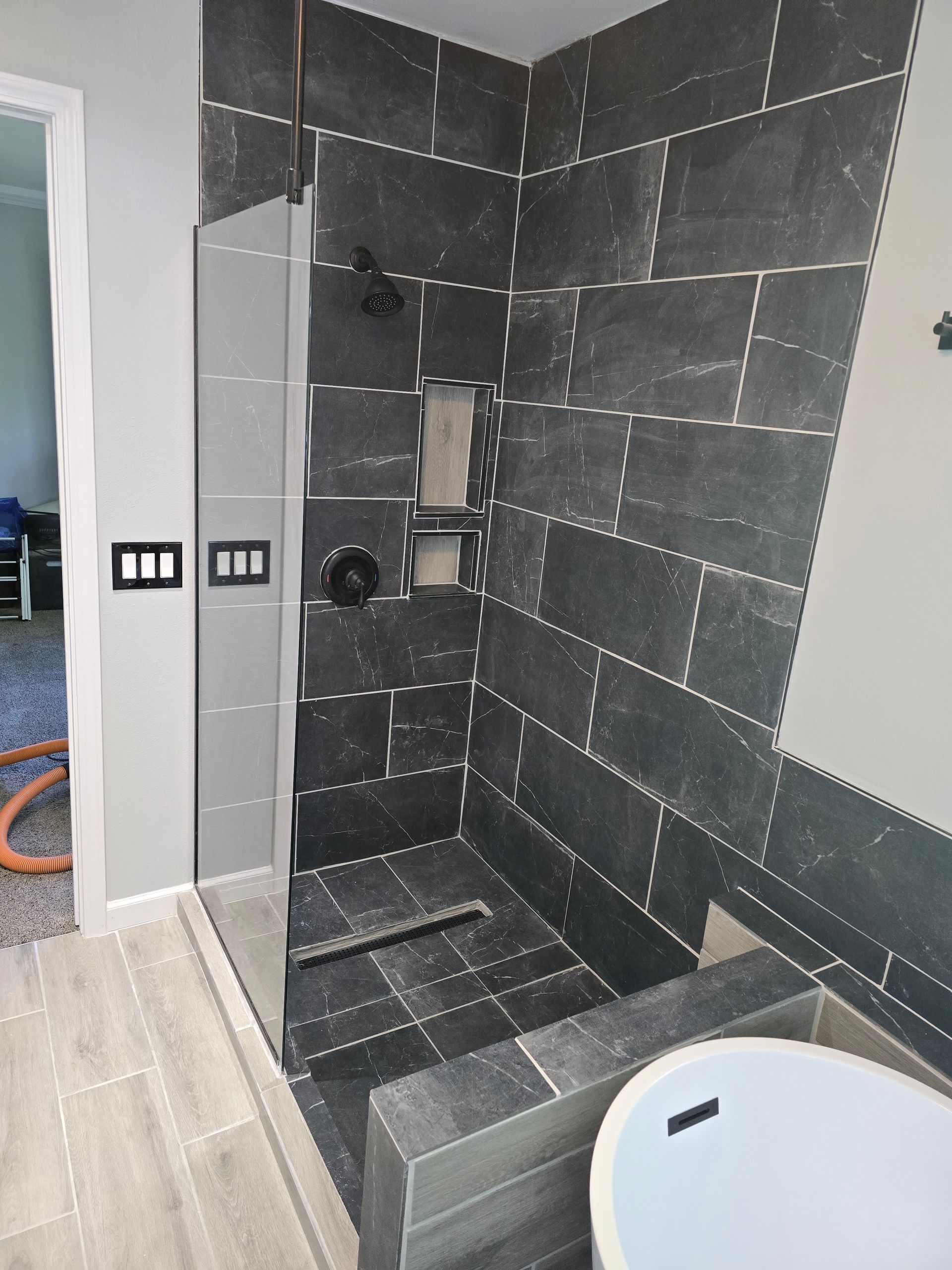 Modern shower with gray tiled walls and floor, glass door, and recessed niches.
