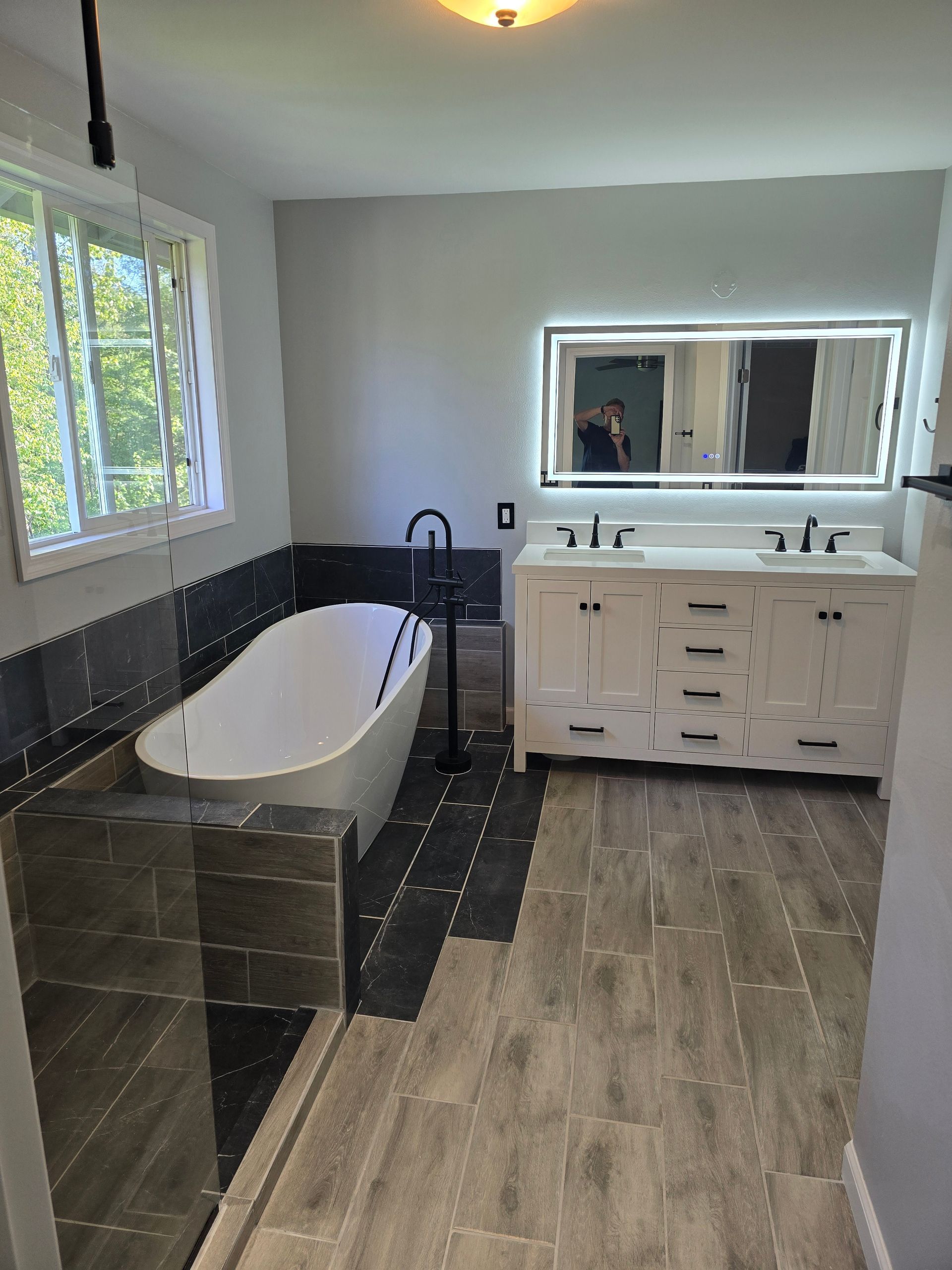 Modern bathroom with a white tub, double vanity, and large mirror. Gray and white color scheme.