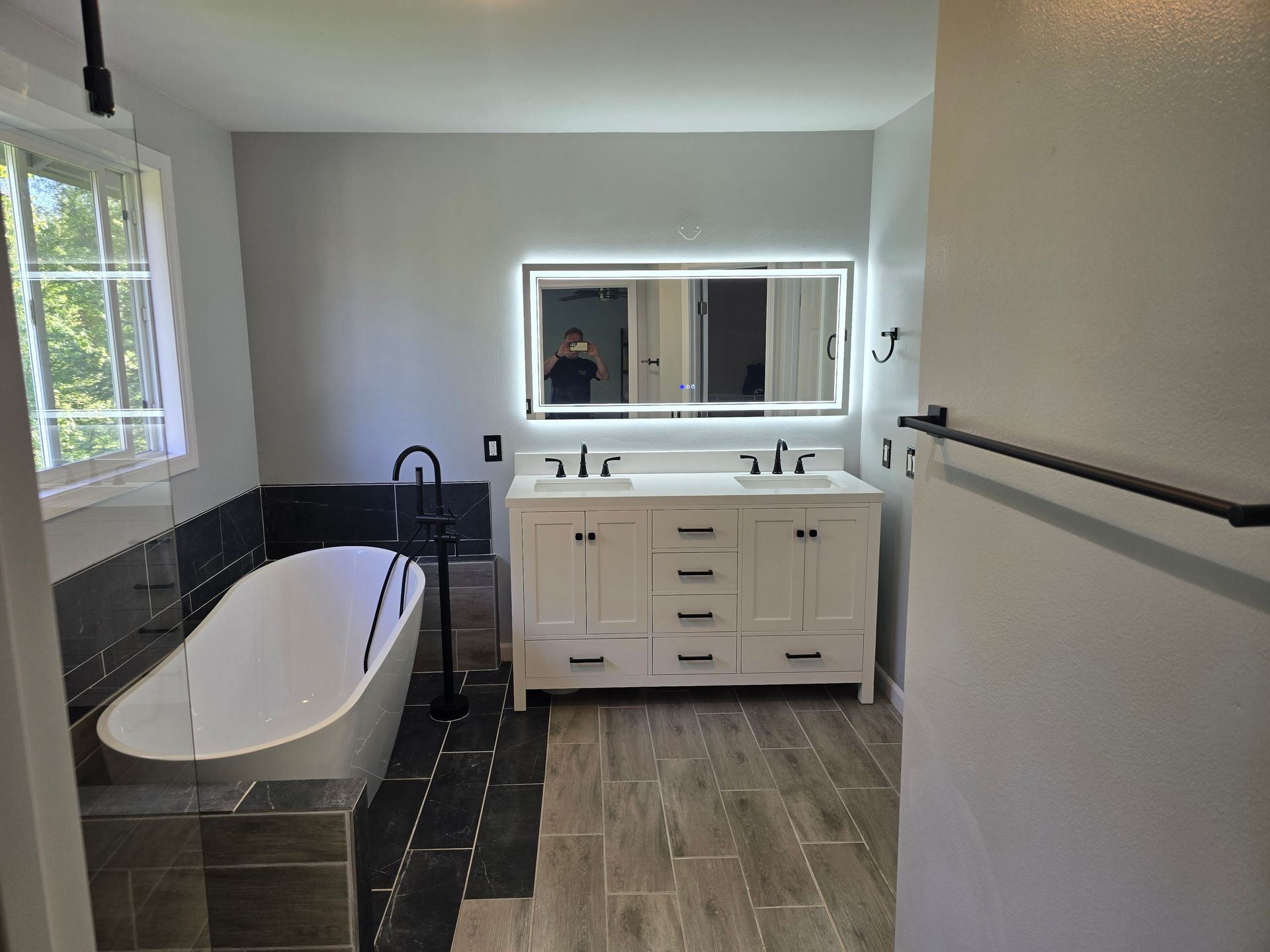 Modern bathroom with white soaking tub, double vanity, and wood-look tile.
