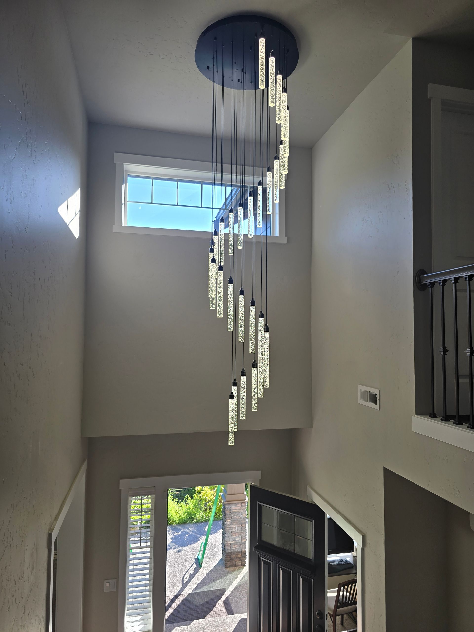Modern spiral chandelier hangs in a two-story entryway, with a window and a front door.