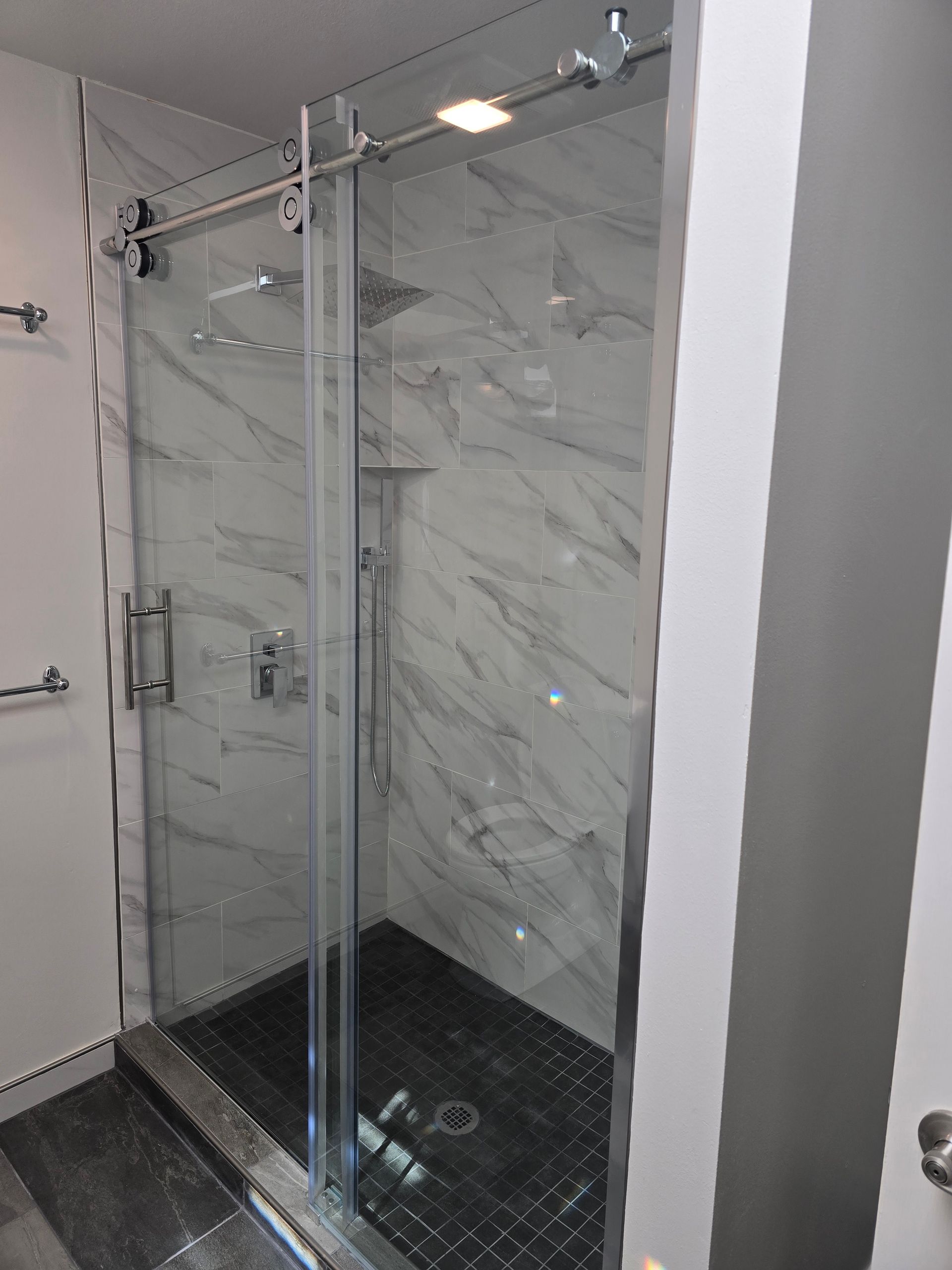 Glass shower enclosure with sliding door and marble-look tile.