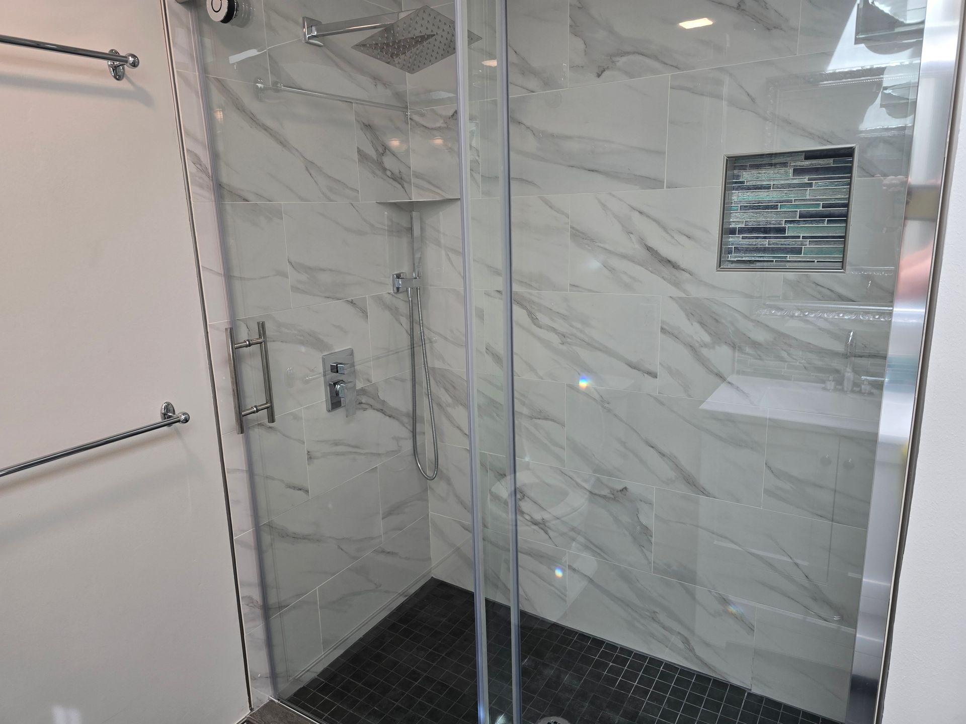 Modern bathroom with a glass shower enclosure and marble-patterned tiles.