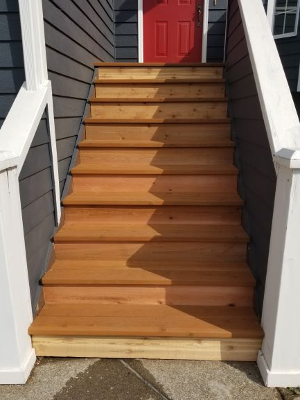 Wooden outdoor staircase leading up to a red door, flanked by white railing posts.
