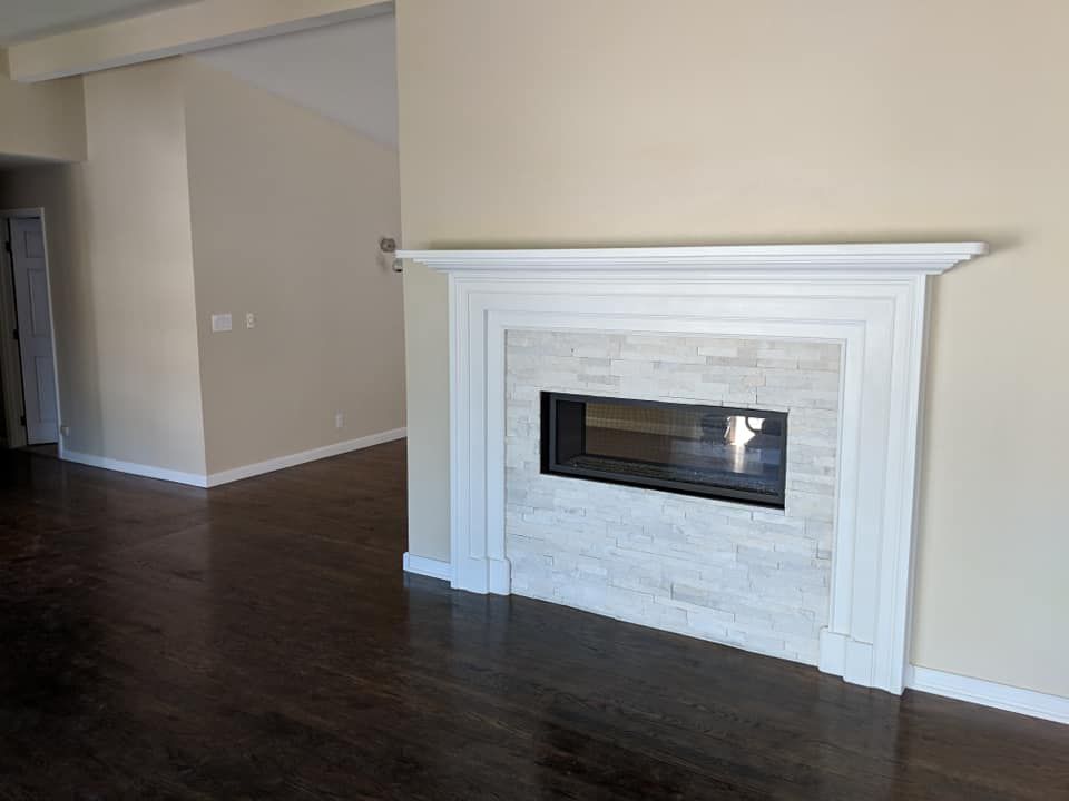 Fireplace with white mantel, light stone tile surround, dark wood floor, beige walls.