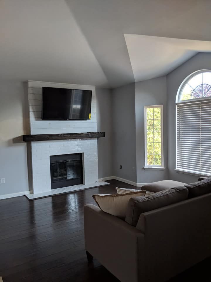 Living room with a fireplace, TV, and couch; walls are gray, floors are dark wood.