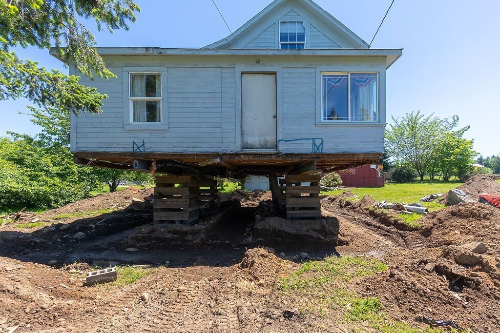 House raised on wooden supports above a dirt lot with construction in progress.
