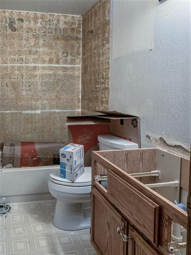 Bathroom undergoing renovation; toilet, tub, and vanity are exposed. Walls have tile removed.