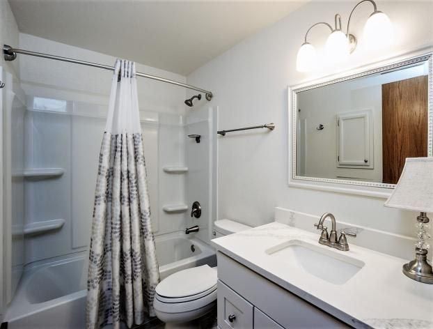 White bathroom with shower, toilet, sink, mirror, and overhead lighting.