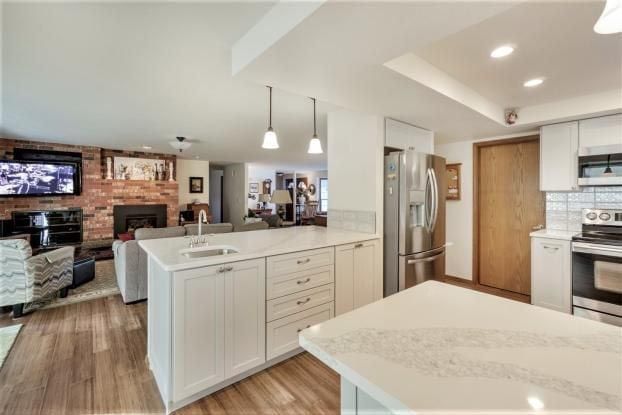 Kitchen with white cabinets, stainless steel appliances, and island, open to living room with brick fireplace.