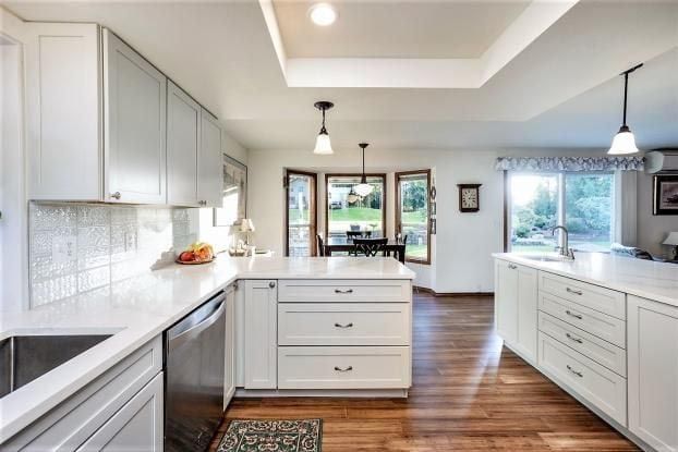 Bright white kitchen with countertops, cabinets, and a central island. Hardwood floors and a window view.