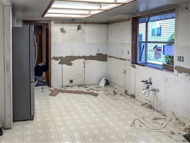 Kitchen interior during renovation with exposed walls, linoleum floor, and a window.