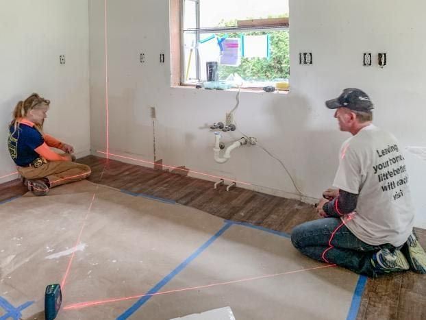 Two people using laser levels in a room with exposed plumbing and construction.