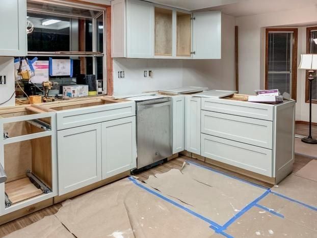 Kitchen undergoing renovation; new white cabinets installed, dishwasher in place, window open.