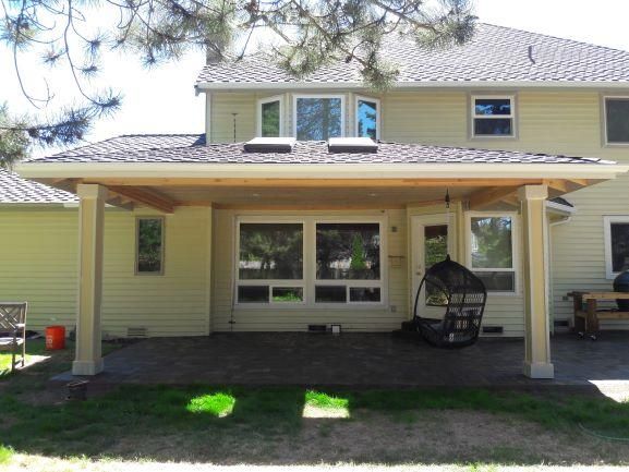 Covered patio attached to a two-story beige house with windows, a lawn, and clear blue sky.