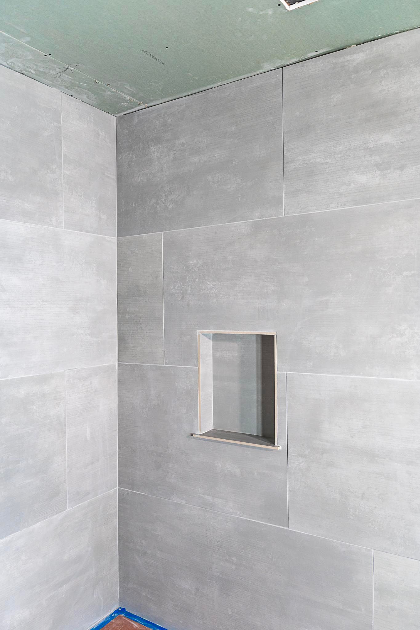 Gray tiled shower with built-in niche. Corner view, ceiling partially visible.