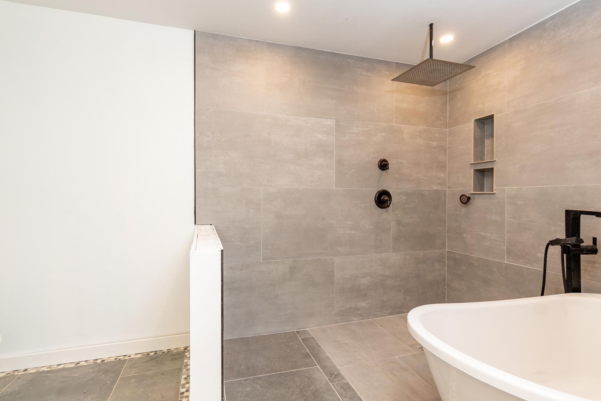 Modern bathroom with gray tile shower and tub, black fixtures, and white walls.