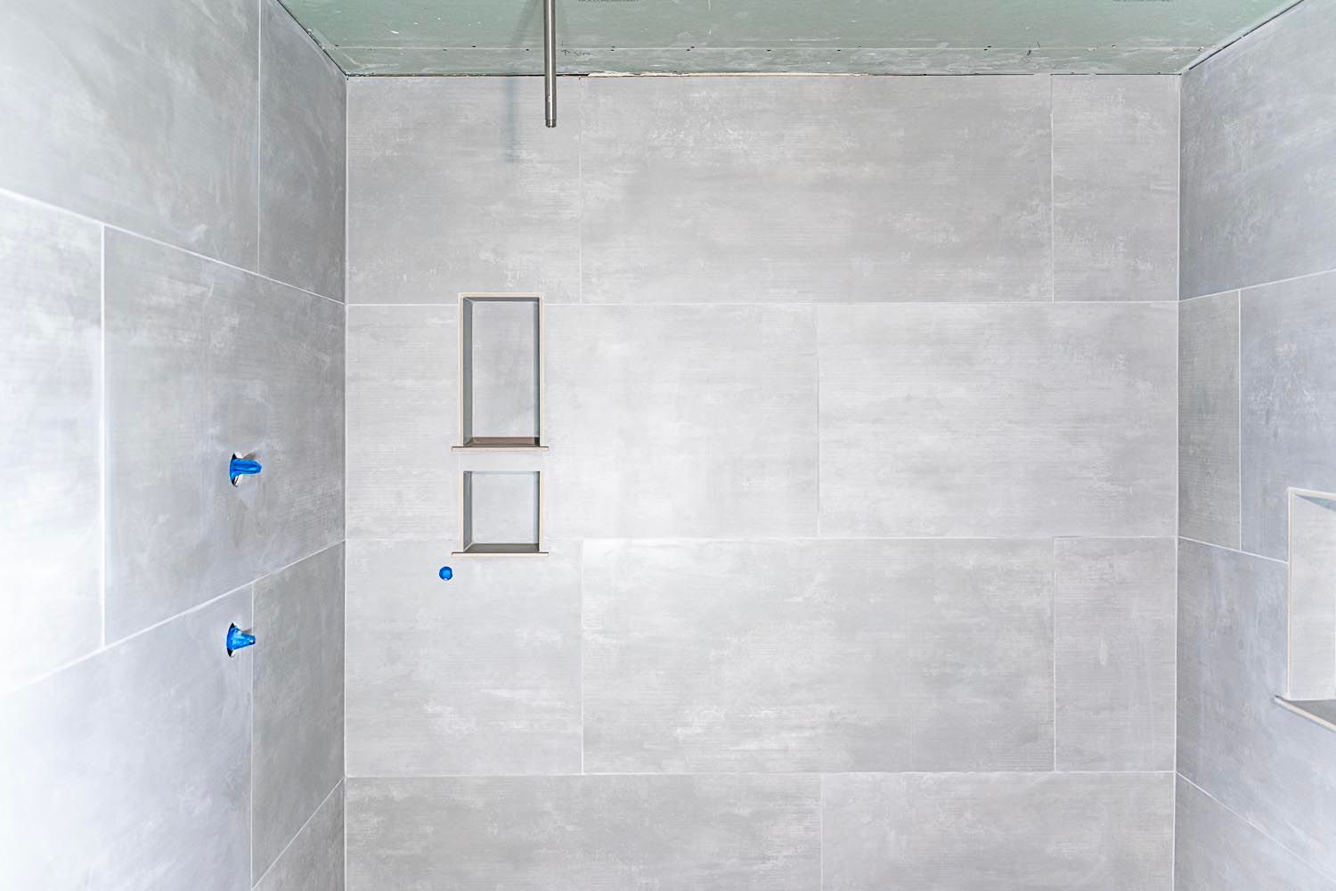 Gray tiled shower stall with built-in shelf and showerhead, in progress.