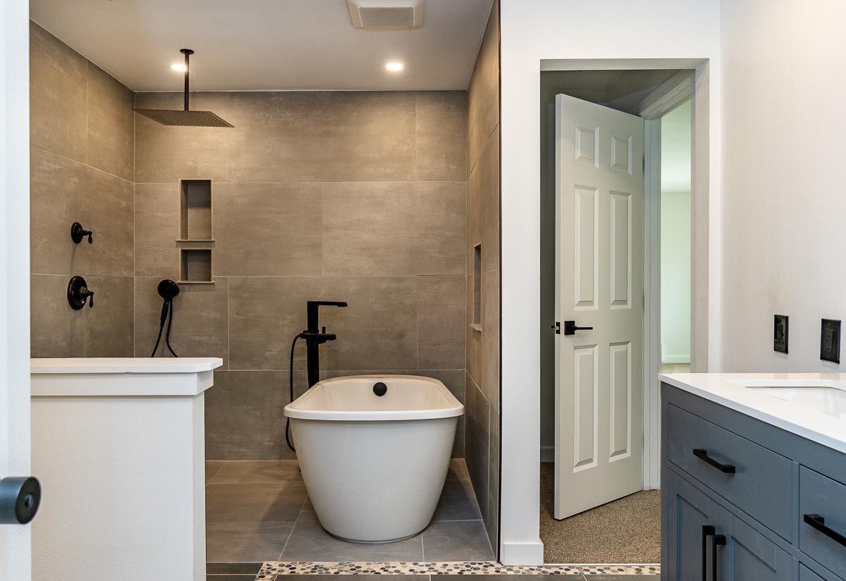 Modern bathroom with grey tiled shower, soaking tub, and open door to the sink area.