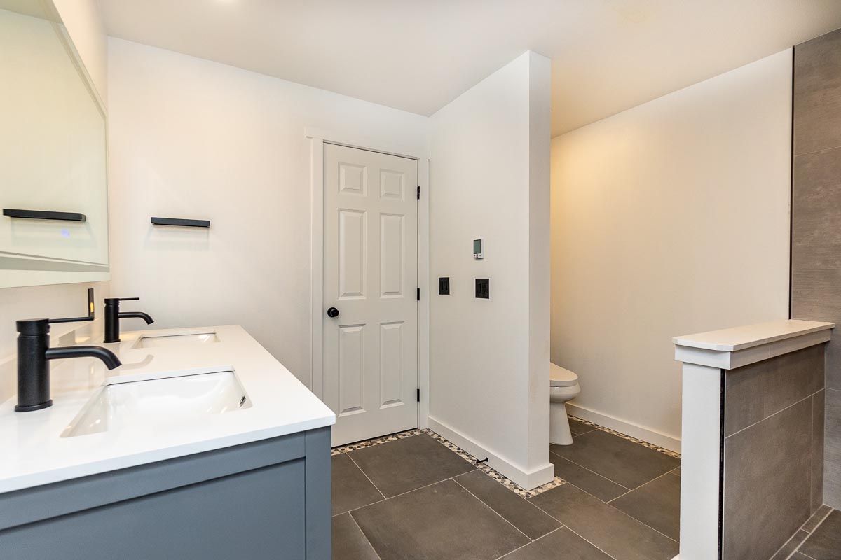 Bathroom with white walls, gray floor, double vanity, and separate toilet area.