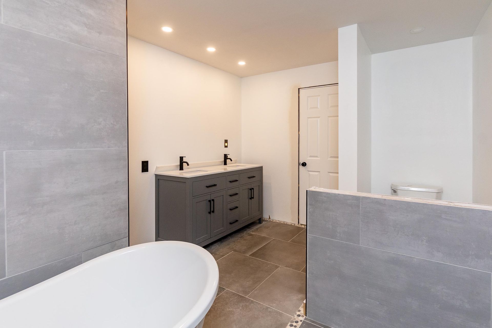 Modern bathroom with gray vanity, white tub, and light gray tiled walls.