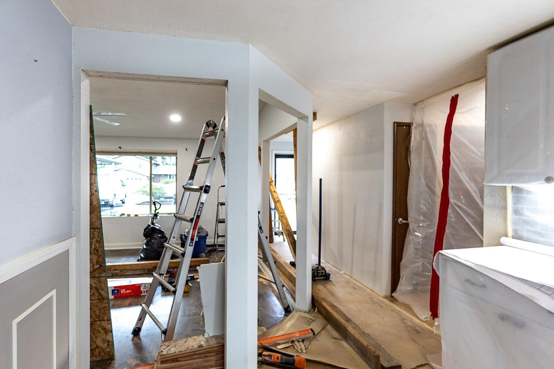 Interior renovation in progress, doorway, hallway, ladder, plastic sheeting, exposed framing, and unfinished walls.