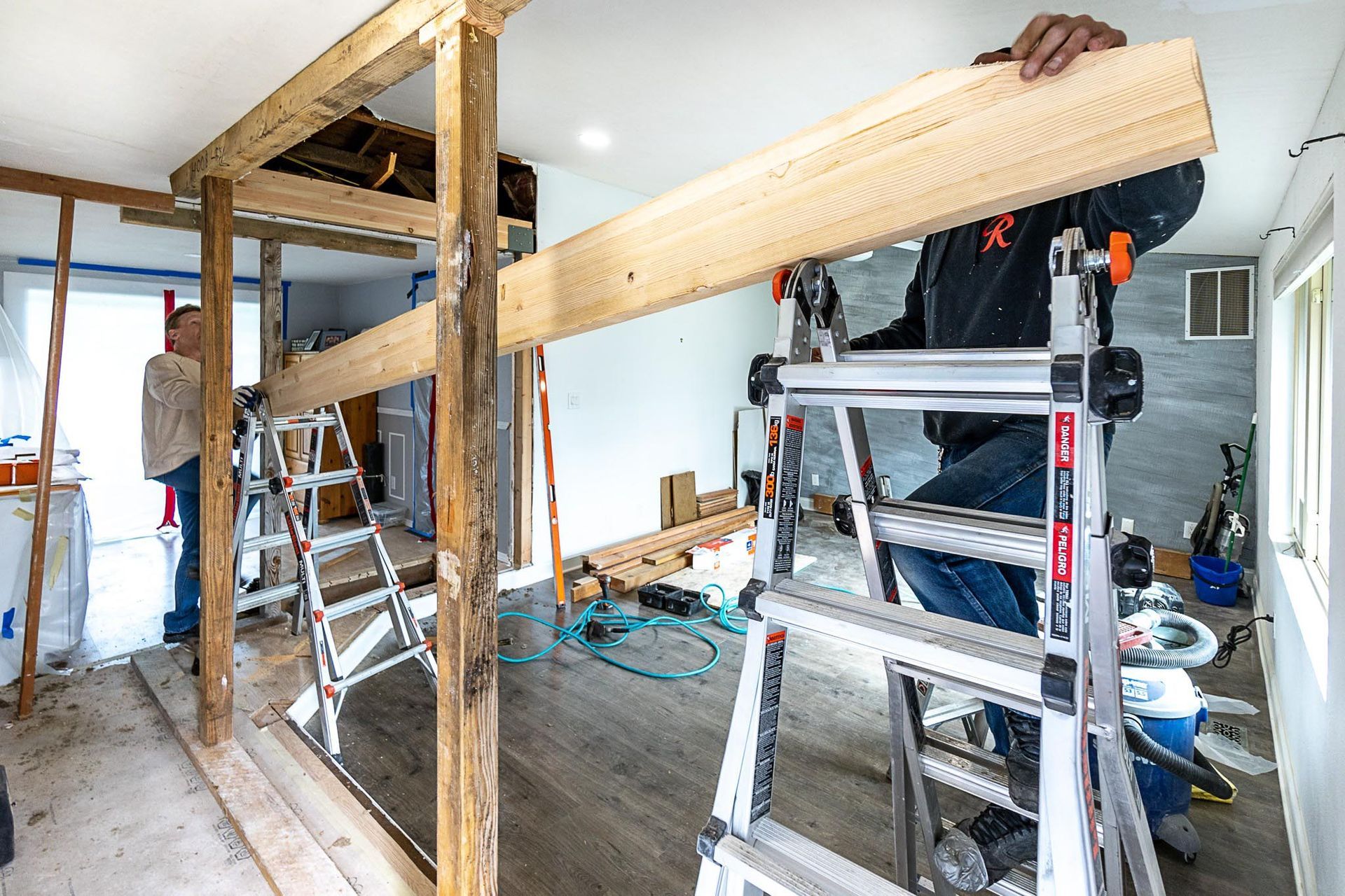 Two people installing a wooden beam during a home renovation. One is on a ladder.