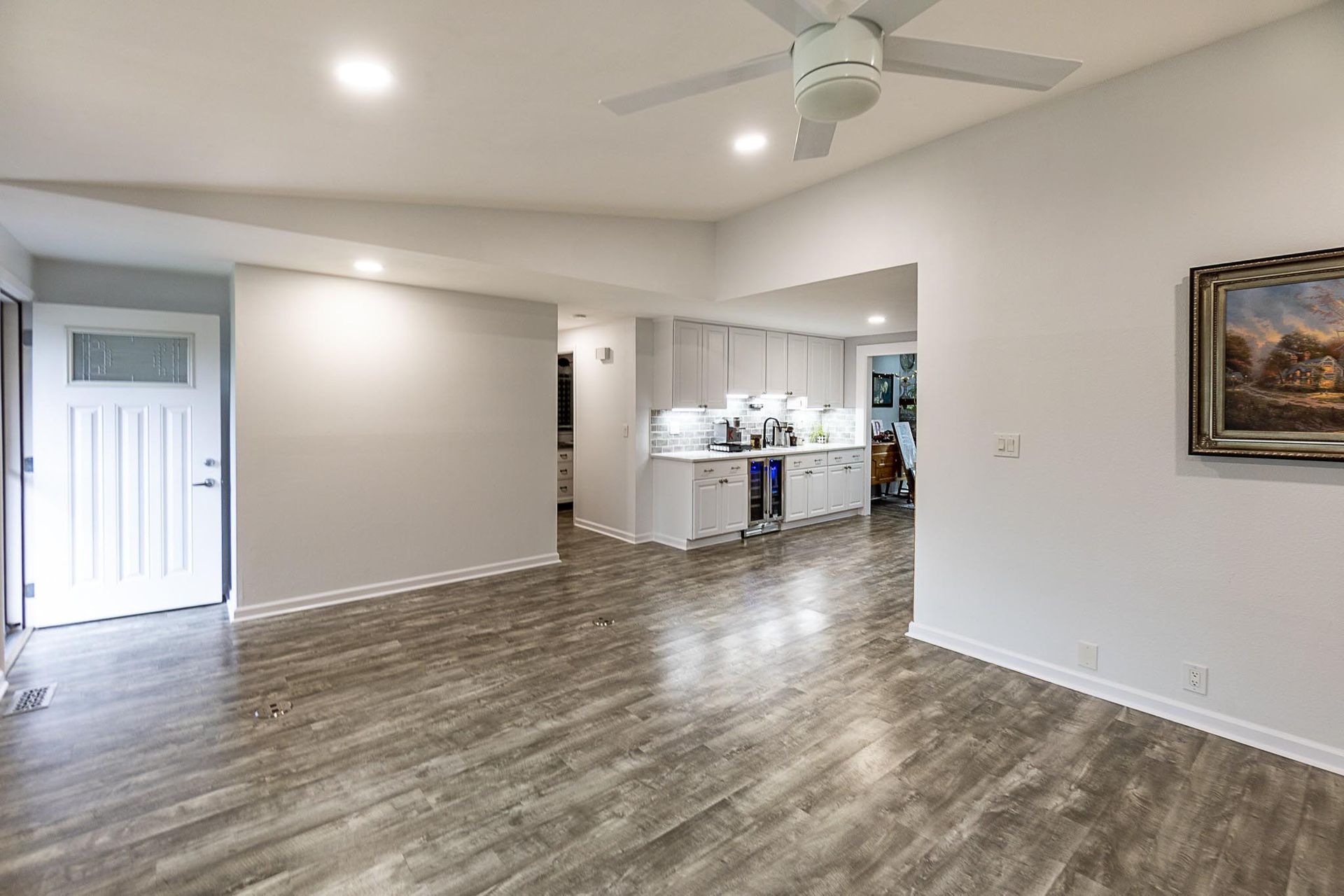 Spacious living room with gray wood floors, white walls, recessed lighting, and a view of the kitchen.