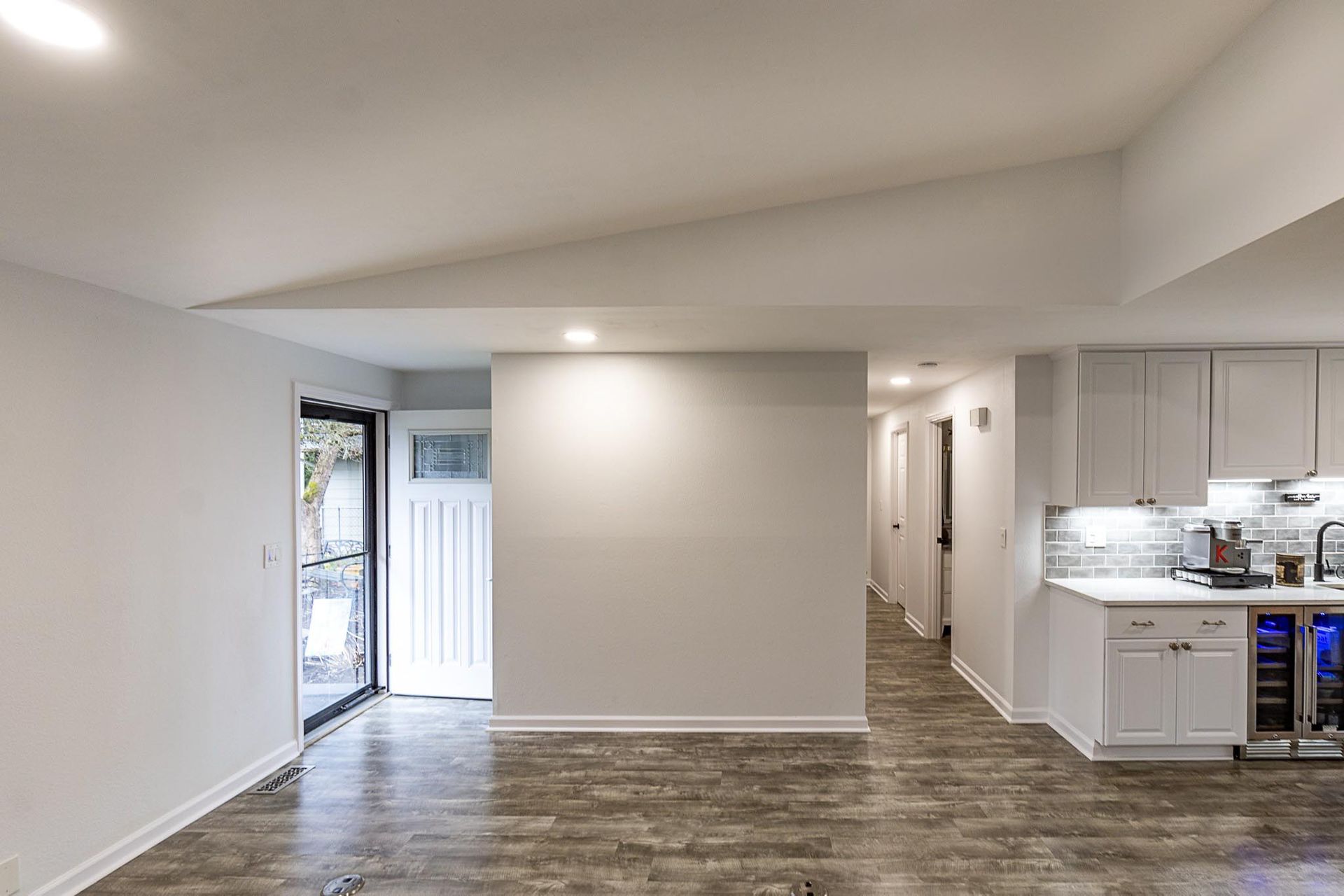 Empty modern apartment living room with open kitchen, white walls, and gray wood flooring