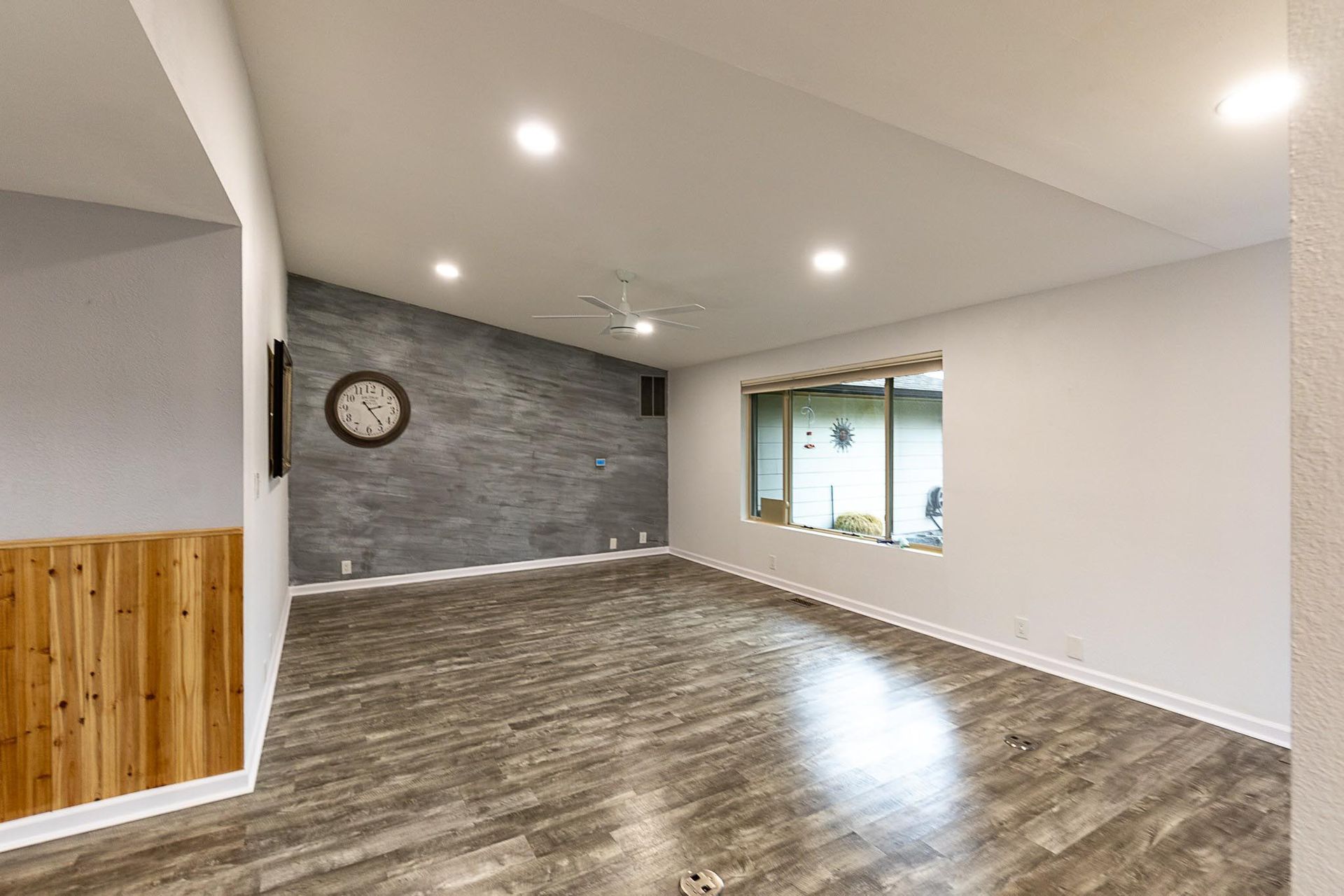 Empty living room with wood-look flooring and textured accent wall, clock, and window.