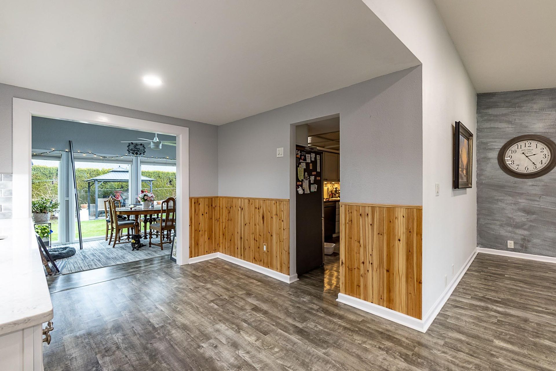 Interior view of a kitchen with gray walls, wood paneling, and a view into a dining area with outdoor access.