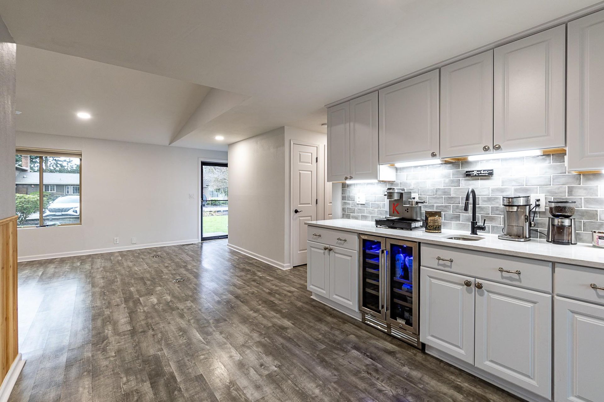 Modern gray and white kitchen with wine cooler, espresso machine, and light wood flooring.
