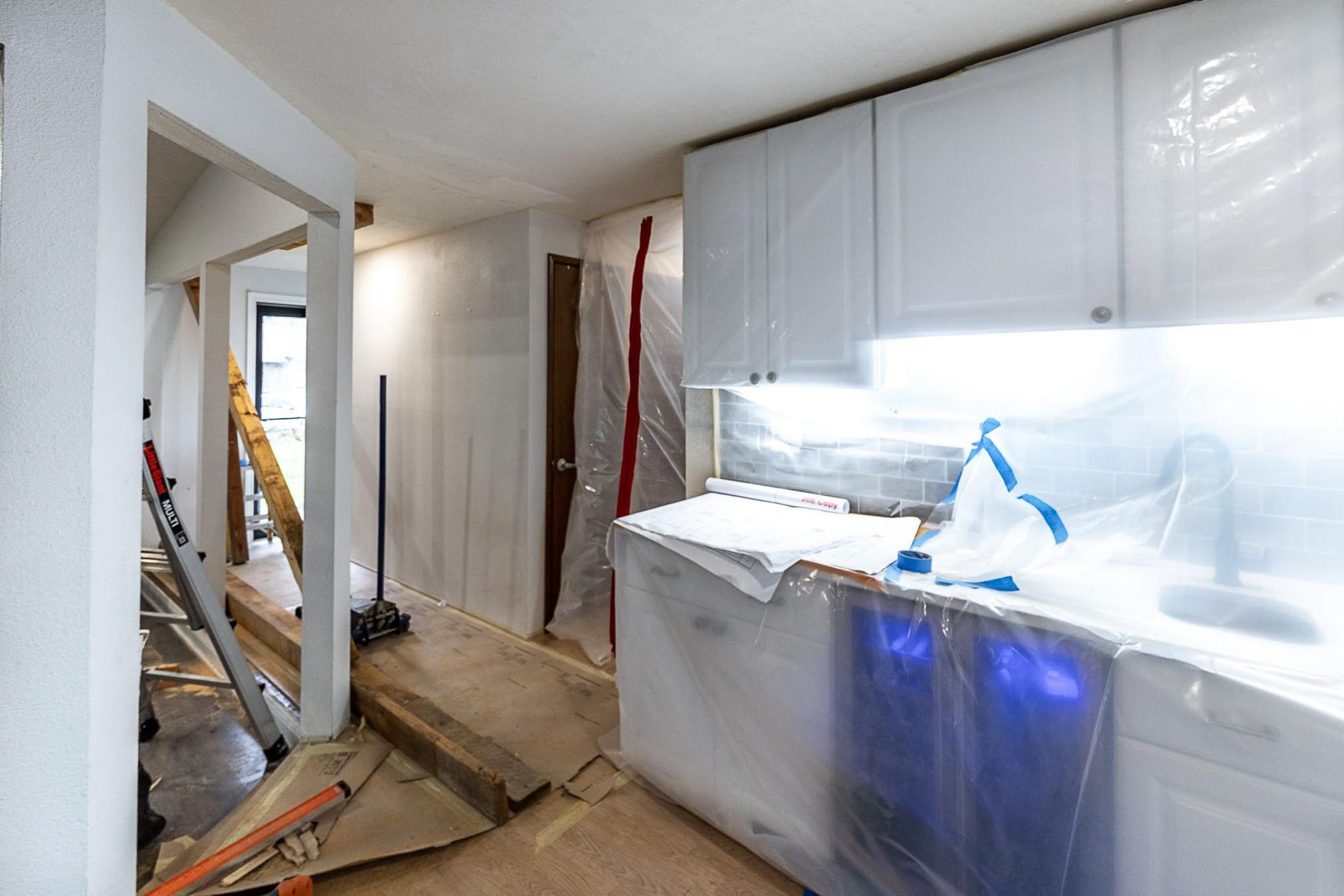 Kitchen under renovation, covered in plastic, with white cabinets and exposed doorway.
