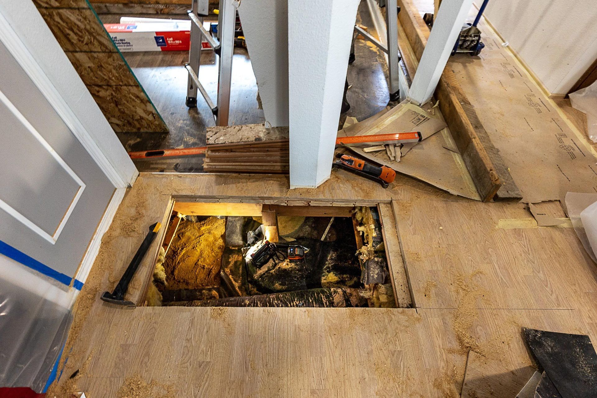Opening in flooring reveals dark space, construction in progress, wood and tools visible.