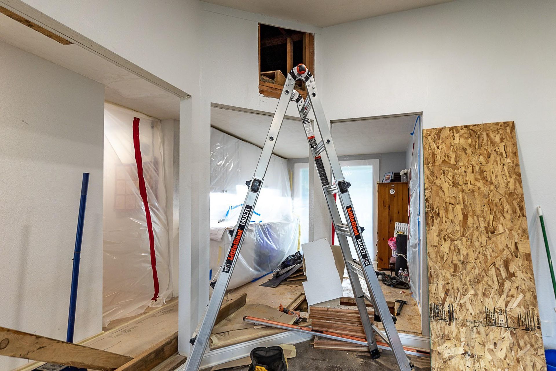 Interior room renovation in progress, featuring ladder, open doorways, and construction materials.